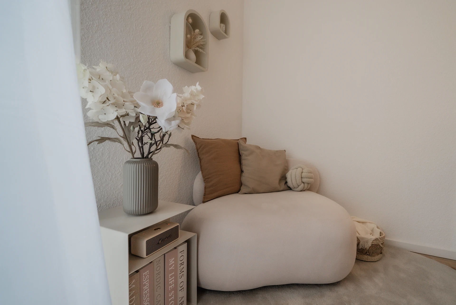 Helle Sitzecke mit Kissen, Blumen und kleinem Beistelltisch.