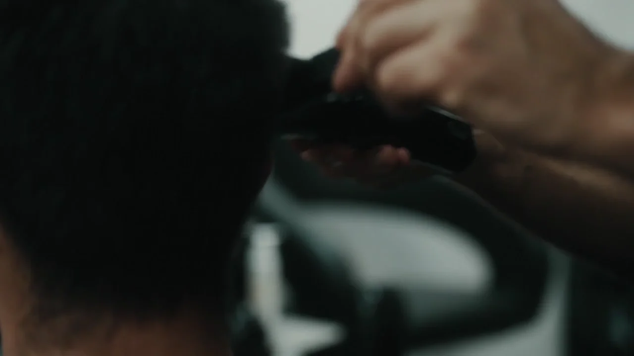 Nahaufnahme: Hände führen den Haarschneider am Hinterkopf entlang.